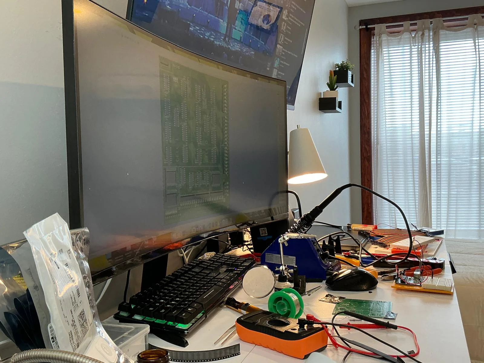 Bench ready for assembly — iron, flux, tweezers, multimeter, and the 07_alu layout on the monitor.